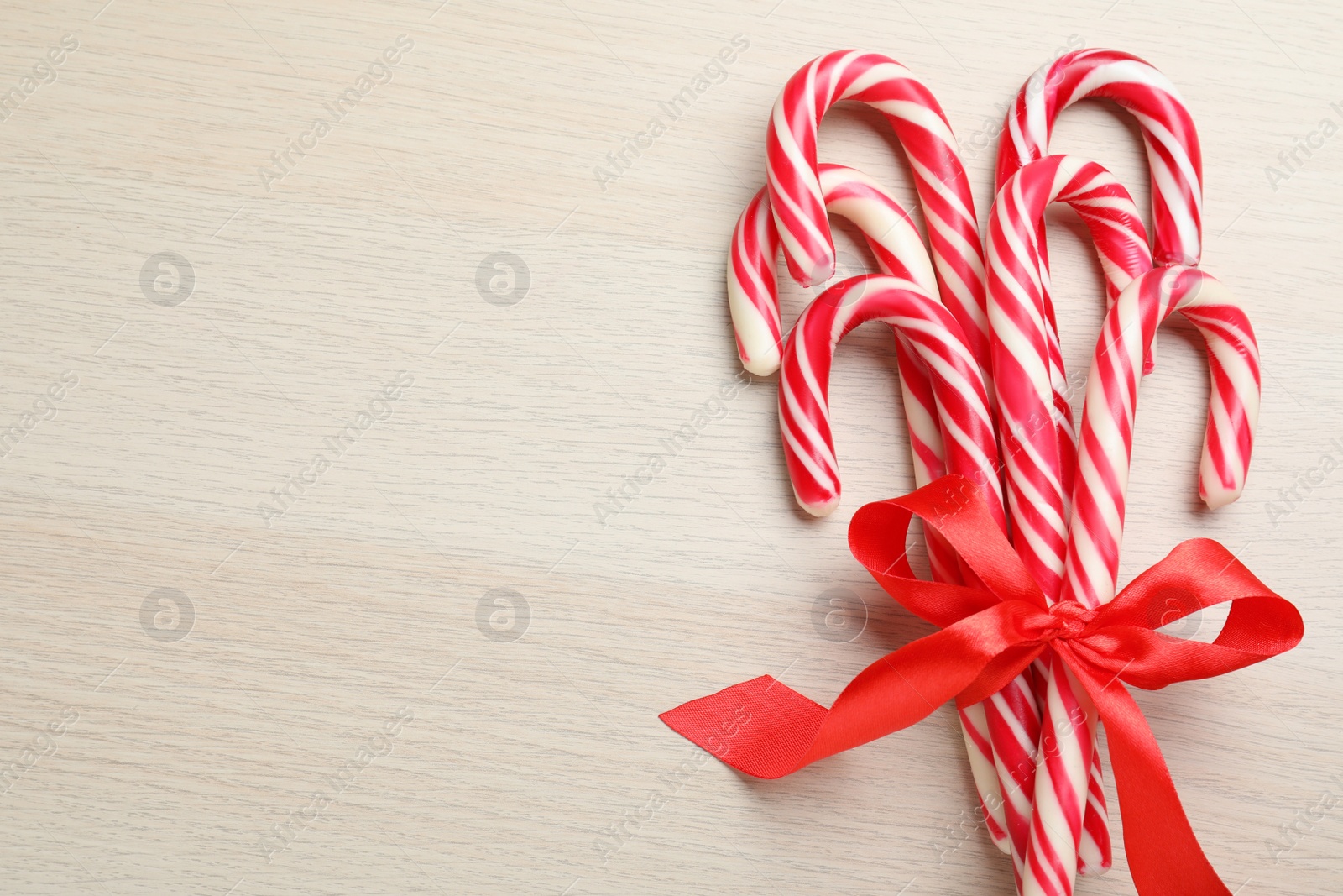 Photo of Sweet Christmas candy canes with red bow on wooden background, top view. Space for text