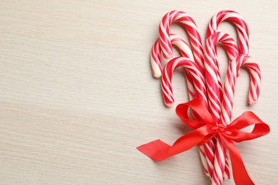 Photo of Sweet Christmas candy canes with red bow on wooden background, top view. Space for text