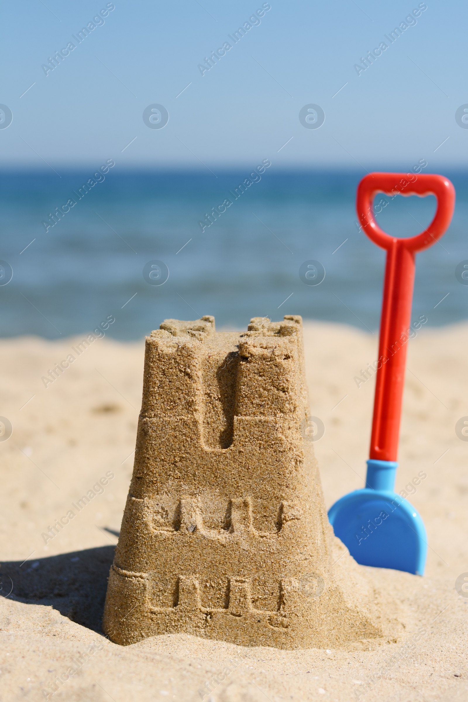 Photo of Sand castle and child plastic shovel on beach near sea