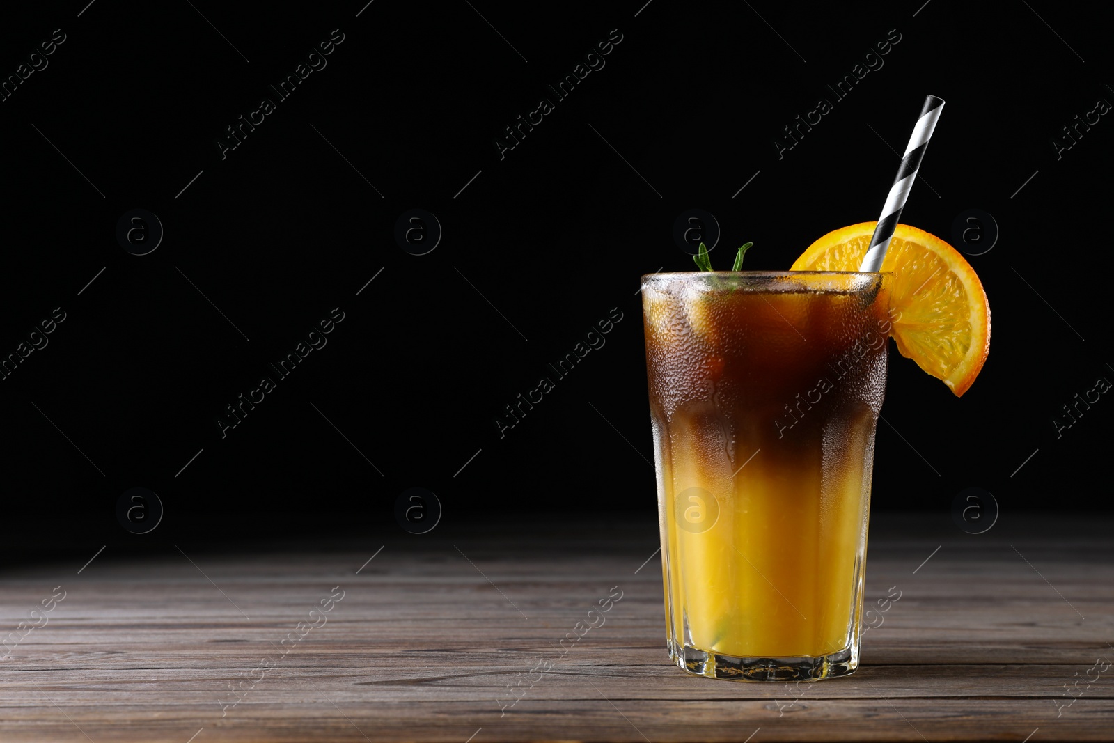 Photo of Tasty refreshing drink with coffee and orange juice on wooden table against dark background, space for text