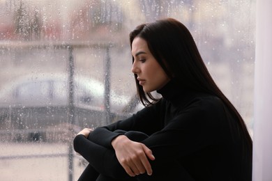 Depressed woman near window on rainy day, space for text