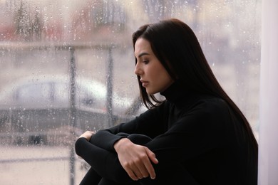 Photo of Depressed woman near window on rainy day, space for text