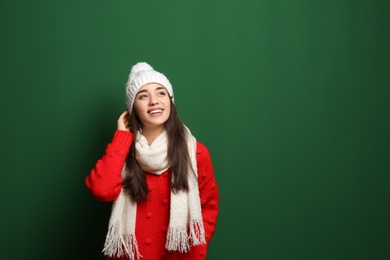 Young woman wearing warm clothes on color background, space for text. Winter season