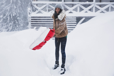 Photo of Young woman cleaning snow with shovel near her house