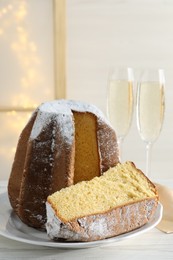 Delicious Pandoro cake decorated with powdered sugar and glasses of sparkling wine on white wooden table. Traditional Italian pastry