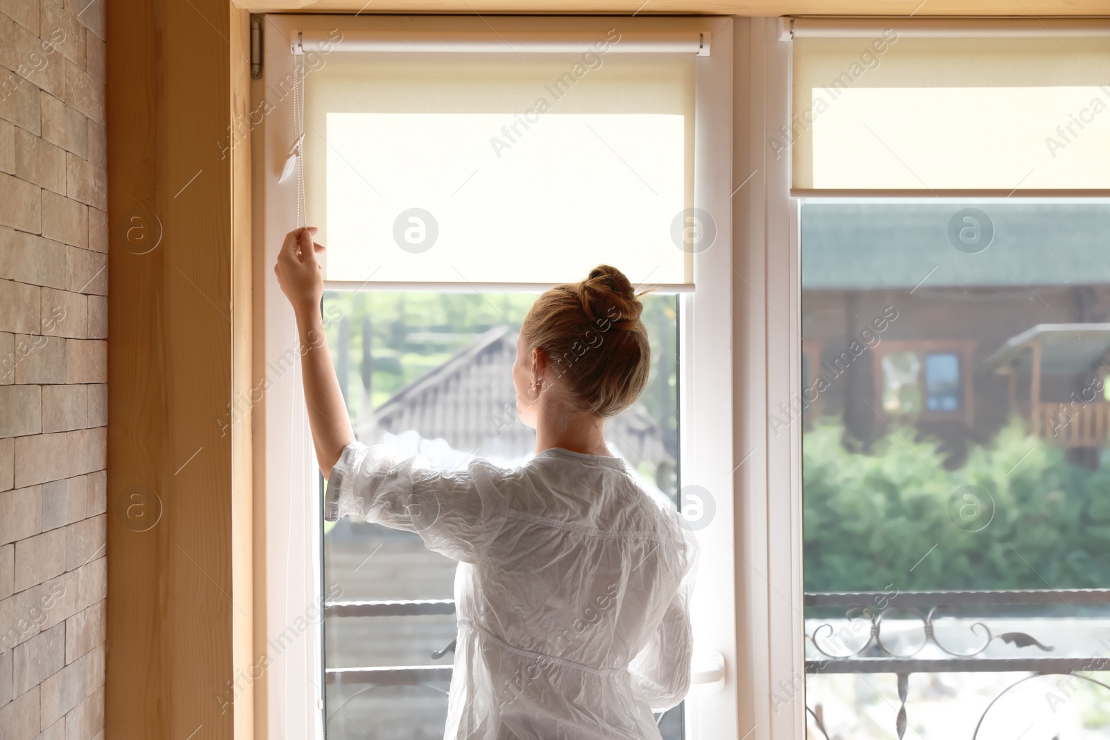 Photo of Young woman opening roller curtains at home