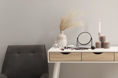 Photo of Dressing table with mirror, cosmetic products, perfumes and burning candles in makeup room