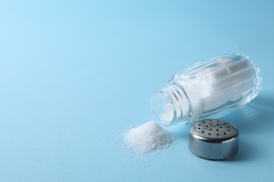 Photo of Organic white salt in shaker on light blue background, closeup. Space for text