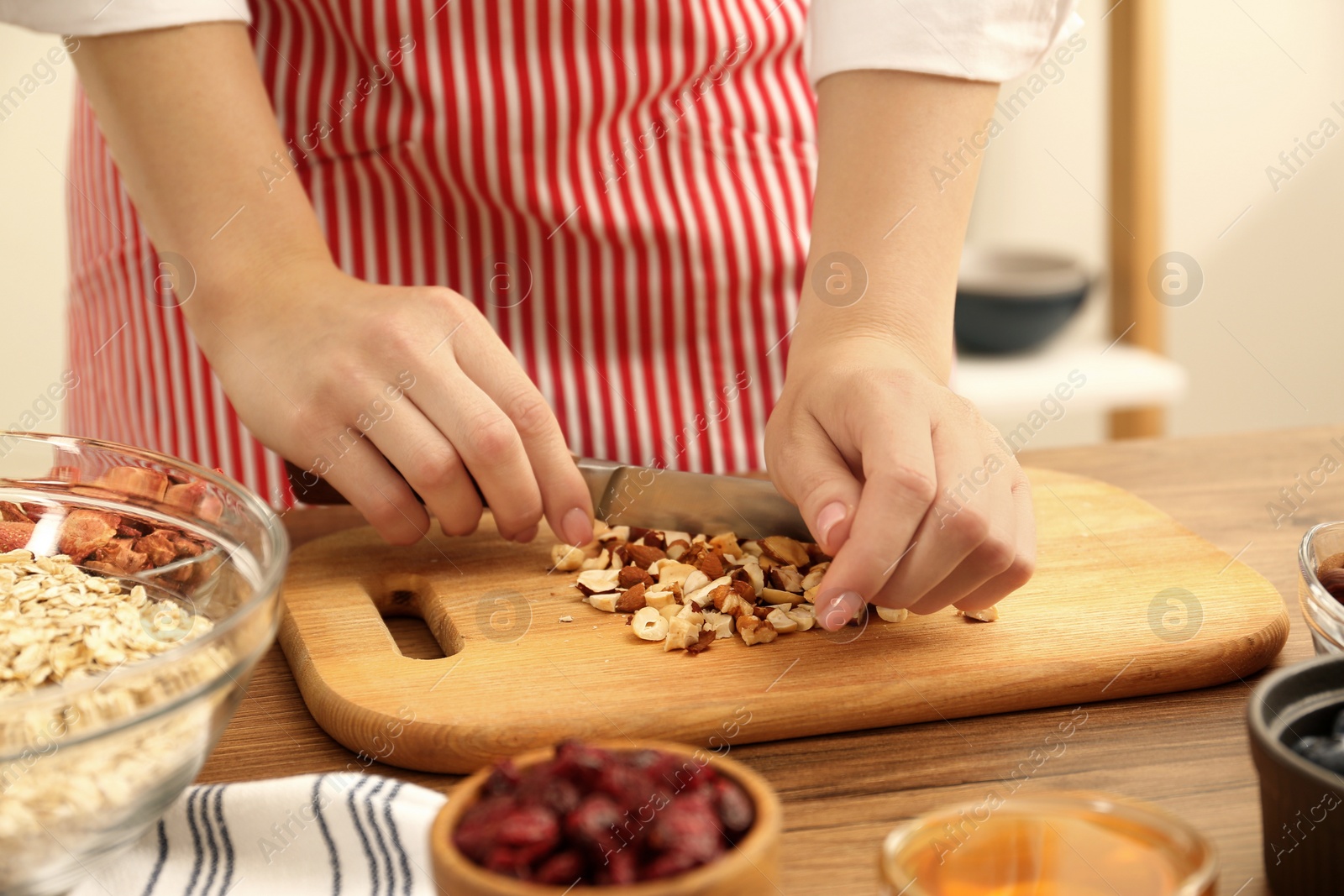 Photo of Making granola. Woman cutting nuts at table in kitchen, closeup