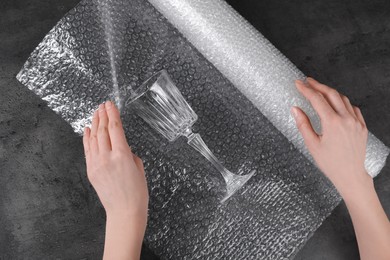 Photo of Woman covering wineglass with bubble wrap at dark grey table, closeup