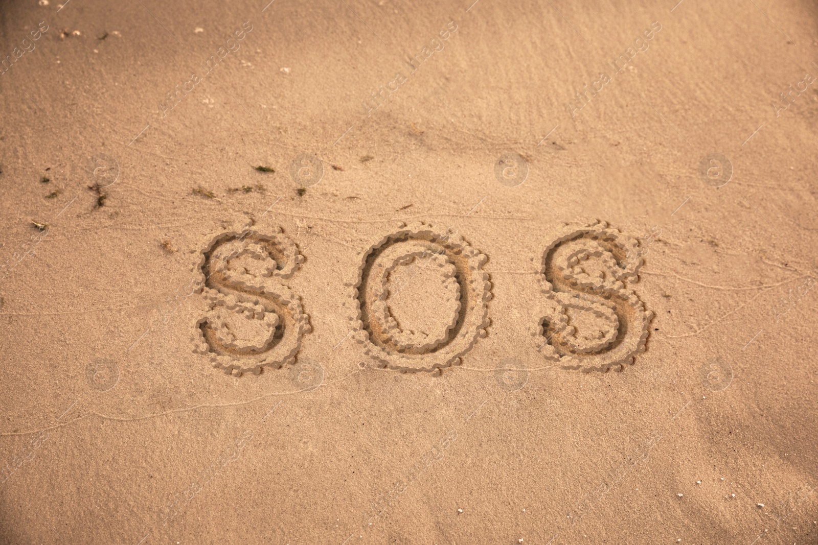 Image of SOS message drawn on sandy beach, top view