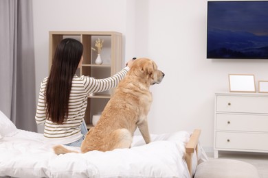 Photo of Happy woman turning on TV while sitting near cute Labrador Retriever at home, back view