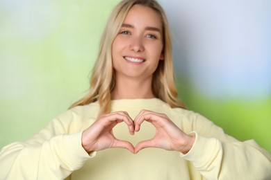 Photo of Beautiful young woman showing heart gesture against blurred background, focus on hands