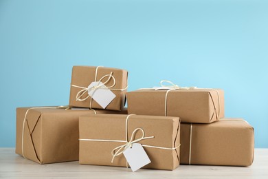 Photo of Parcels wrapped in kraft paper with tags on white wooden table against light blue background