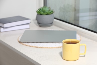 Photo of Cup of tea, laptop, books and succulent on wooden window sill