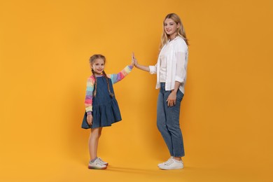 Photo of Mother and daughter giving high five on orange background