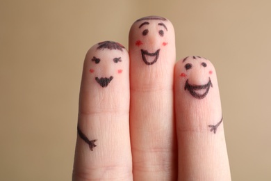 Three fingers with drawings of happy faces on brown background