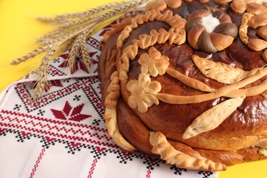 Photo of Rushnyk with korovai on yellow background, closeup. Ukrainian bread and salt welcoming tradition