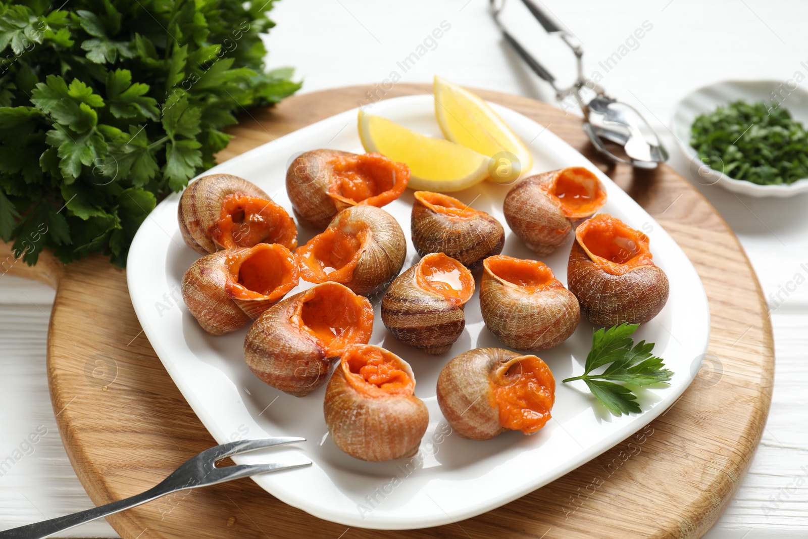 Photo of Delicious cooked snails served on white wooden table