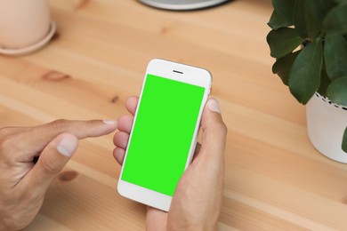 Chroma key compositing. Man using smartphone with green screen at wooden table indoors, closeup. Mockup for design