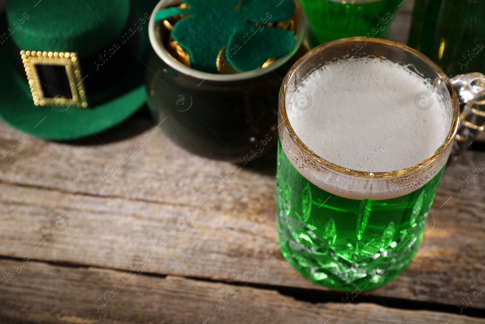 Photo of St. Patrick's day party. Green beer, leprechaun hat, pot of gold and decorative clover leaf on wooden table. Space for text