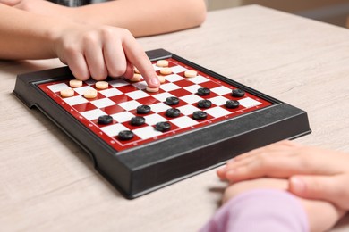 Children playing checkers at light wooden table, closeup