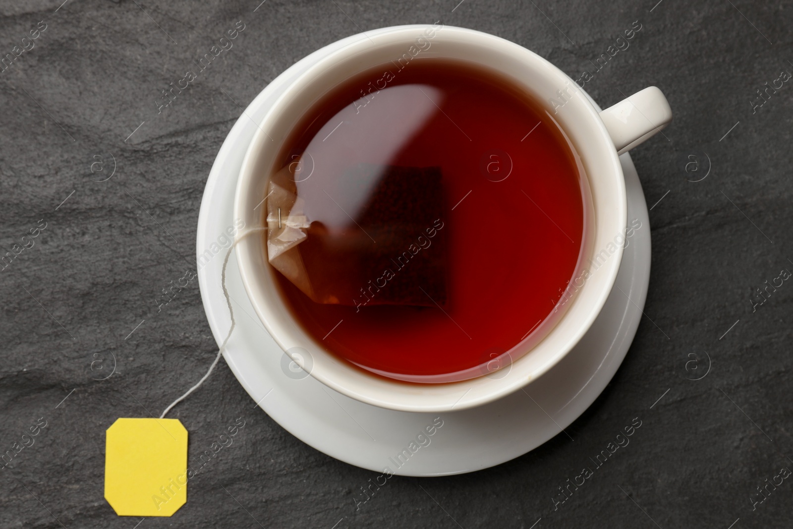 Photo of Tea bag in cup with hot drink on grey textured table, top view