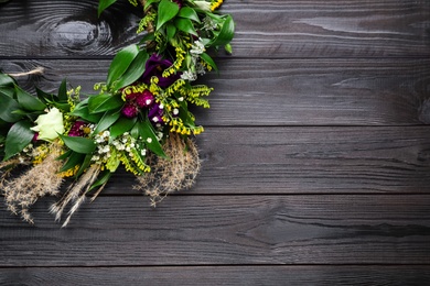 Beautiful wreath made of flowers and leaves on wooden table, top view. Space for text