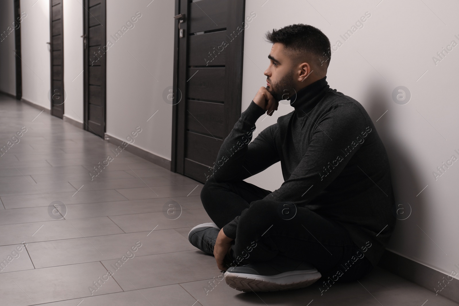 Photo of Sad man sitting on floor in hall. Space for text