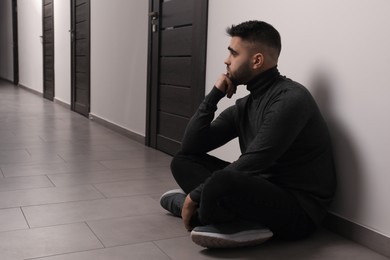 Photo of Sad man sitting on floor in hall. Space for text