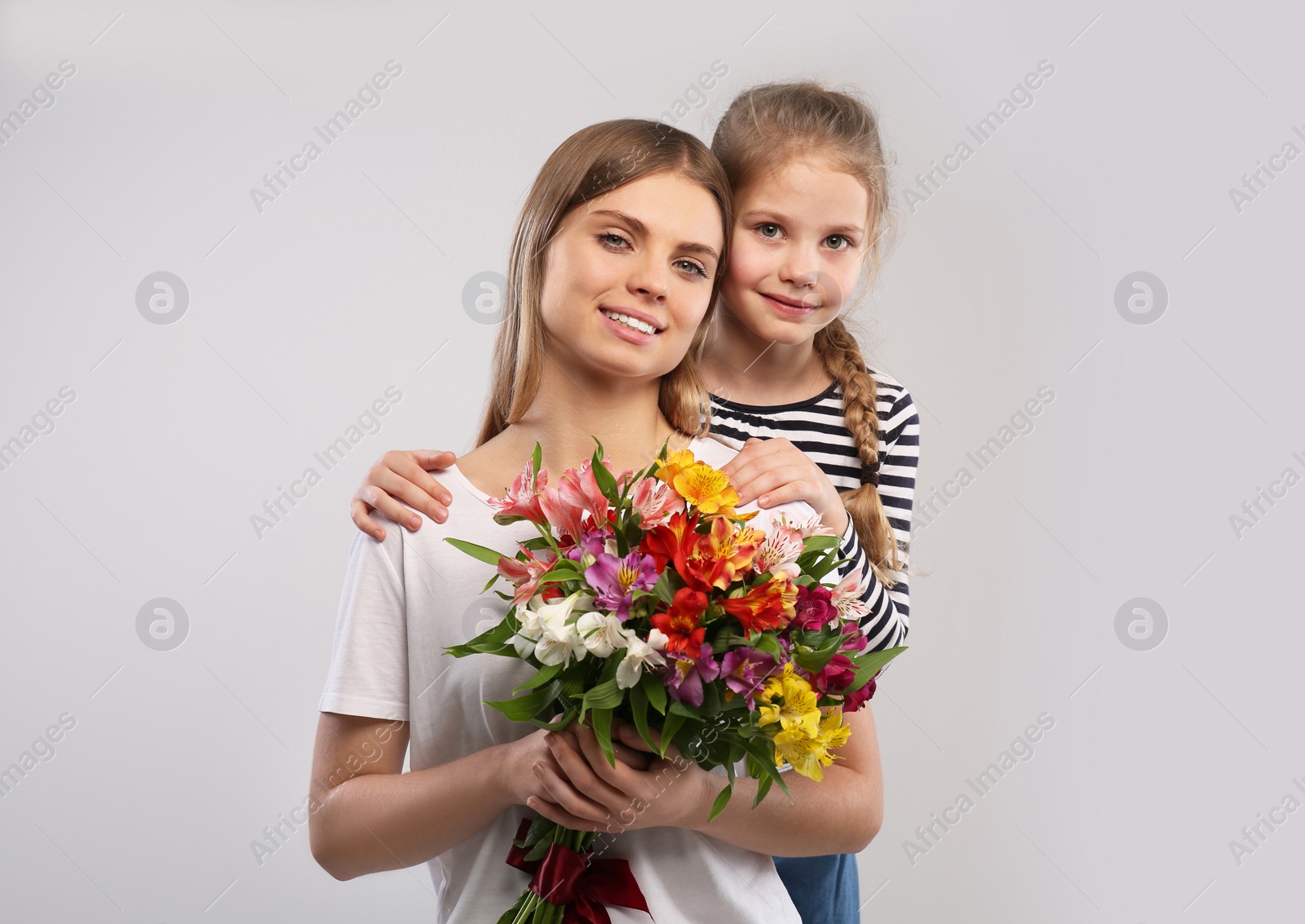 Photo of Little daughter congratulating her mom with flowers on white background. Happy Mother's Day