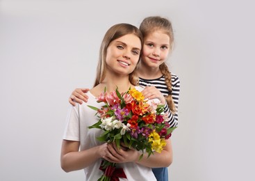 Little daughter congratulating her mom with flowers on white background. Happy Mother's Day