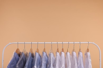 Photo of Dry-cleaning service. Many different clothes in plastic bags hanging on rack against beige background, space for text