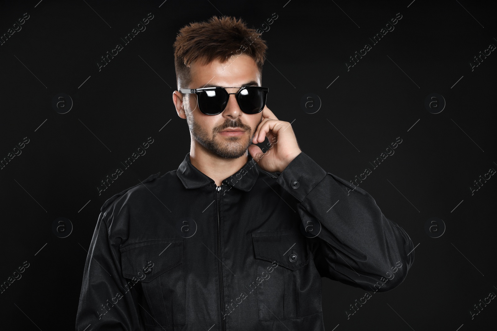 Photo of Male security guard in uniform using radio earpiece on dark background