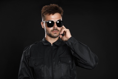 Male security guard in uniform using radio earpiece on dark background