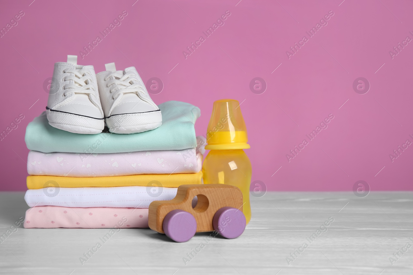 Photo of Children's shoes, stack of clothes and toy on white wooden table. Space for text