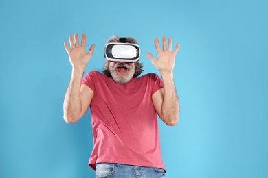 Emotional mature man playing video games with virtual reality headset on color background