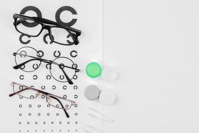 Photo of Vision test chart, glasses, lenses and tweezers on white background, flat lay. Space for text