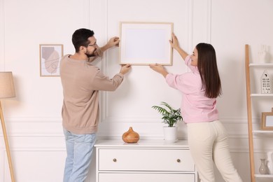 Man and woman hanging picture frame on white wall at home