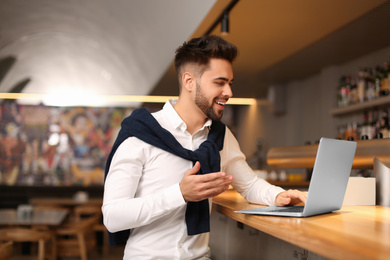 Photo of Young male business owner working with laptop at counter in his cafe