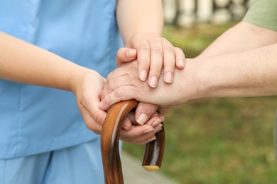 Elderly woman with walking cane and female caregiver outdoors, closeup