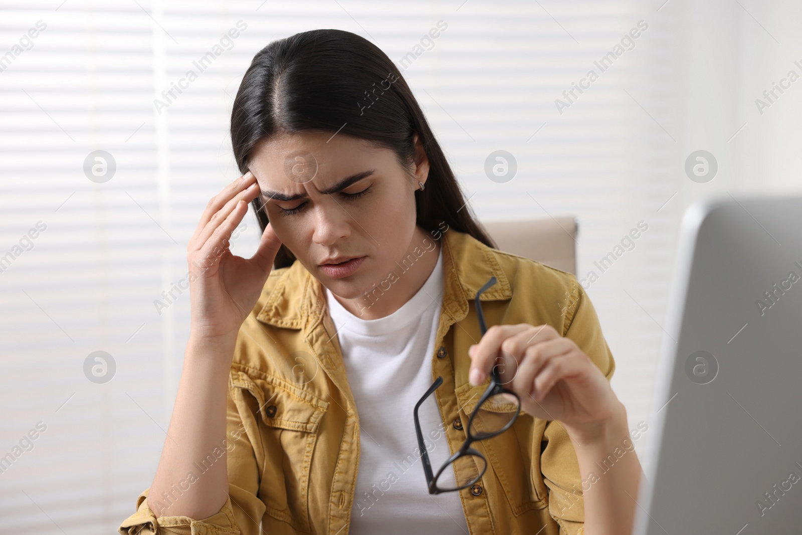 Photo of Young woman suffering from headache at workplace indoors
