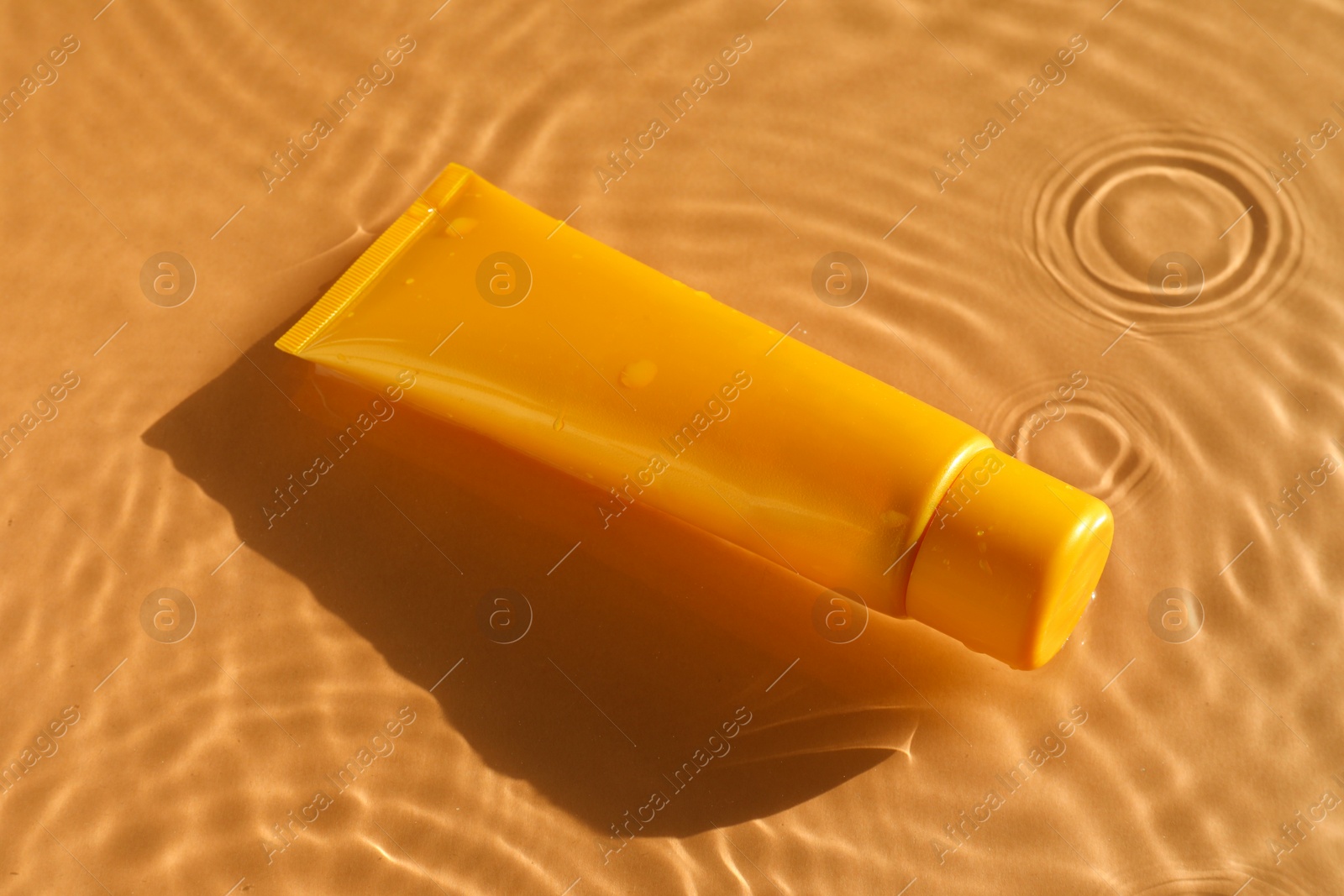 Photo of Tube with moisturizing cream in water on orange background