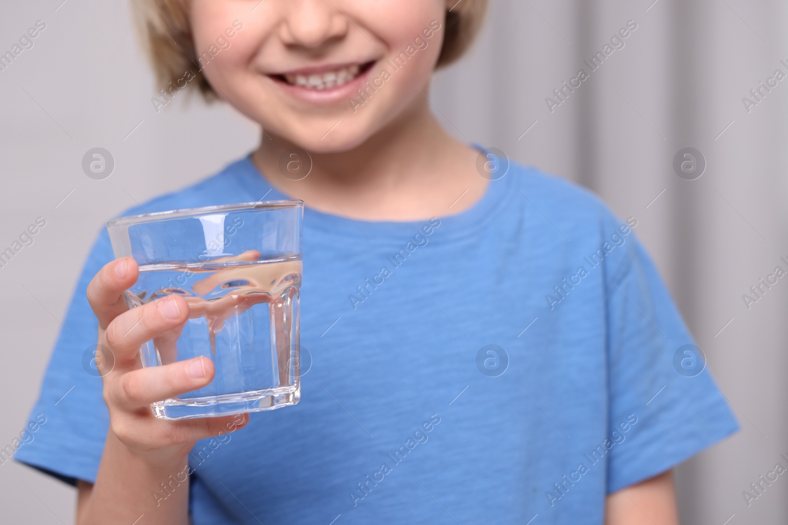 Photo of Little boy holding glass of fresh water indoors, closeup