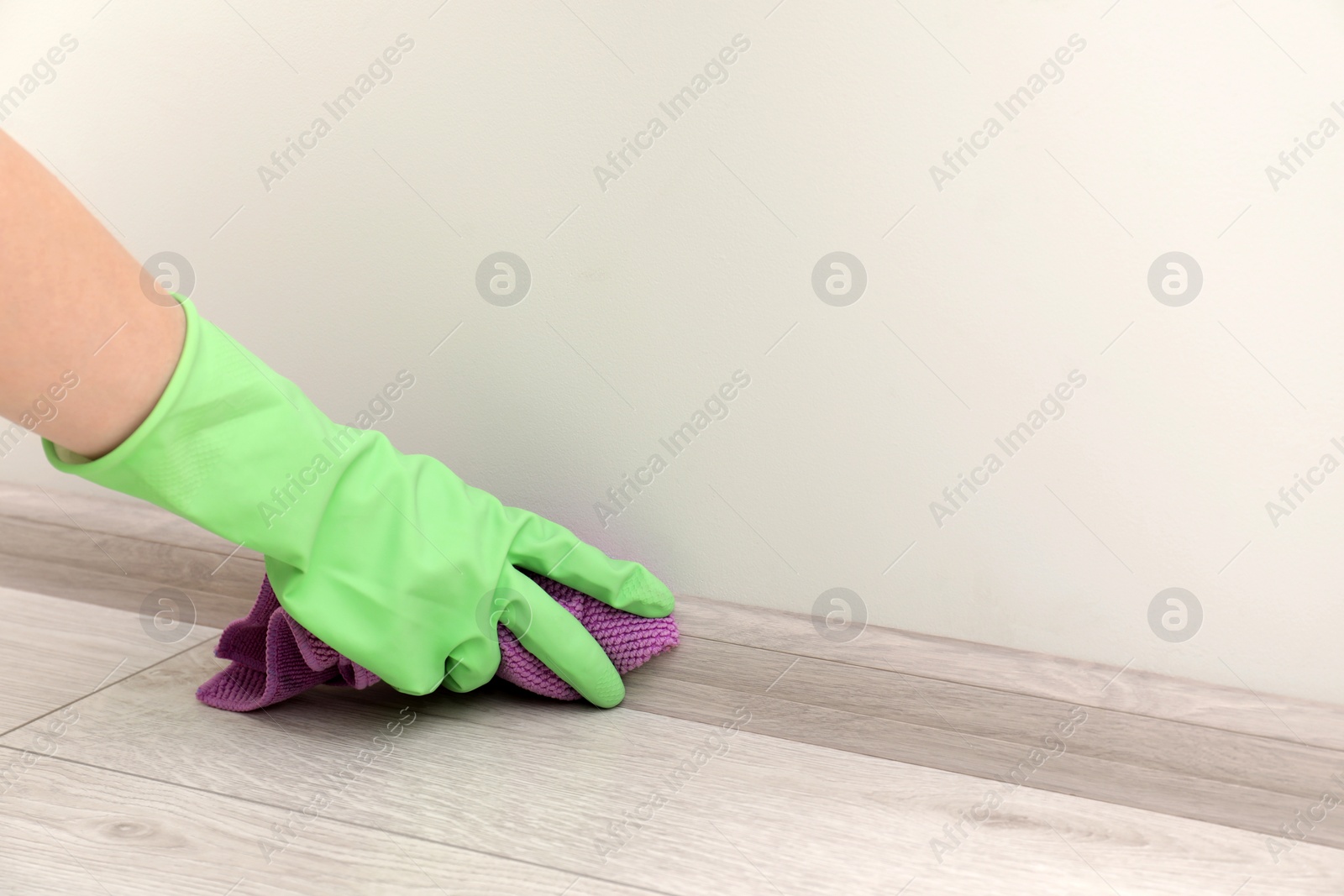 Photo of Woman in protective glove cleaning plinth with washcloth indoors, closeup. Space for text