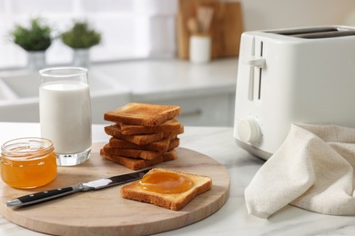 Breakfast served in kitchen. Toaster, crunchy bread, honey and milk on white table
