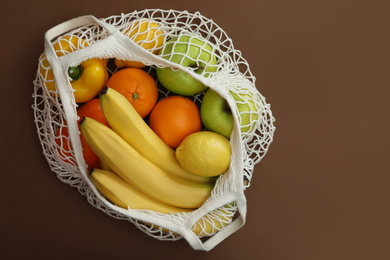 Net bag with fruits and vegetables on brown background, top view