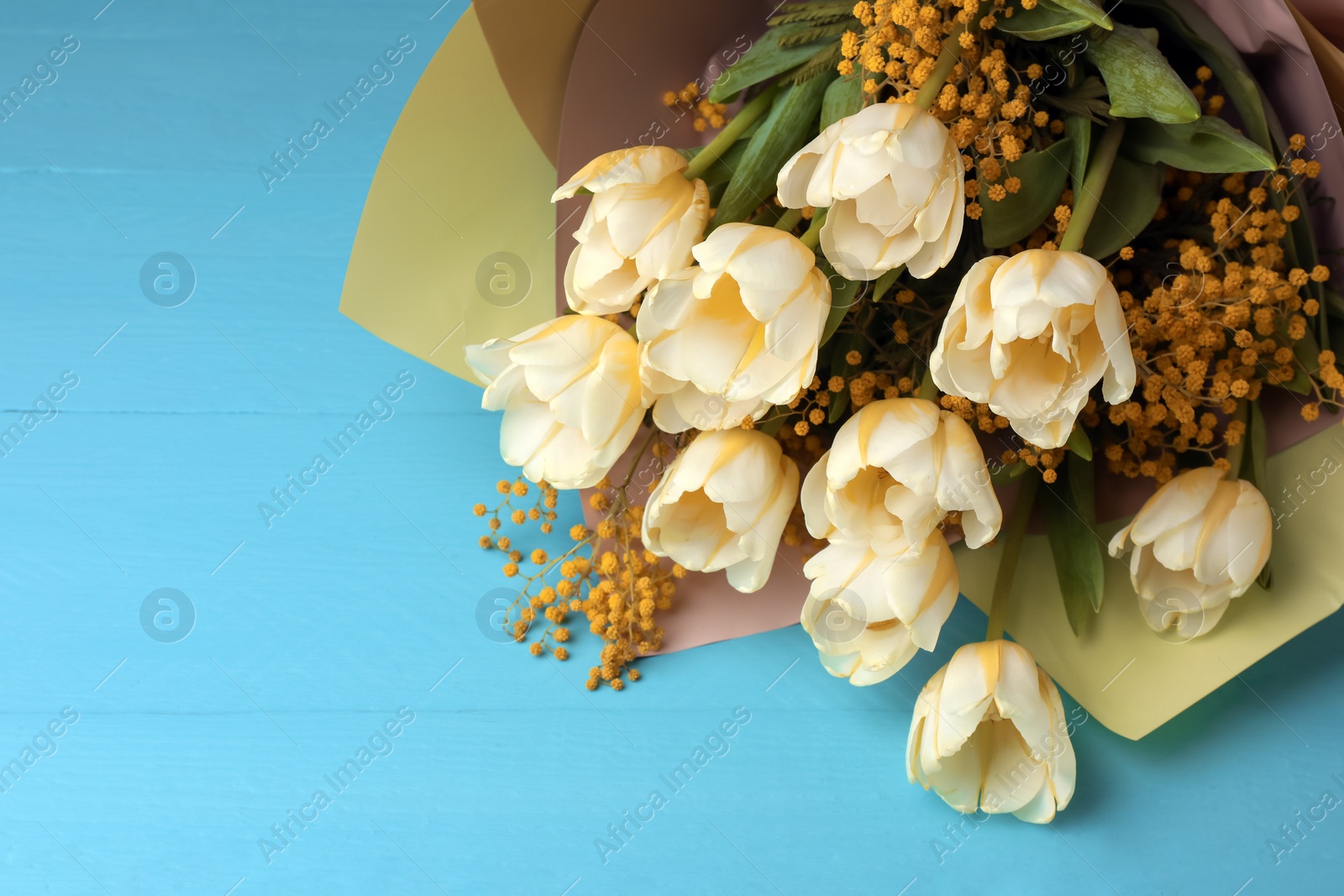 Photo of Bouquet with beautiful tulips and mimosa flowers on light blue wooden table. Space for text