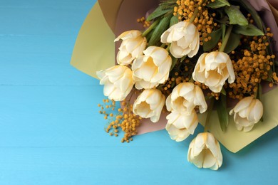 Bouquet with beautiful tulips and mimosa flowers on light blue wooden table. Space for text