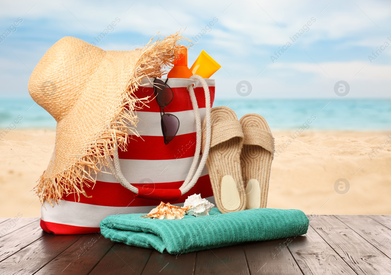 Image of Stylish bag with beach accessories on wooden surface near seashore